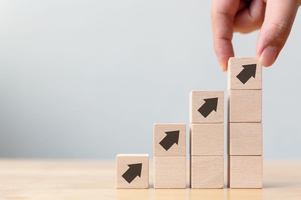 Ręka układająca ostatni klocek w rosnącym wykresie z drewnianych kostek ze strzałkami w górę – metafora rozwoju biznesu we współpracy z WPT